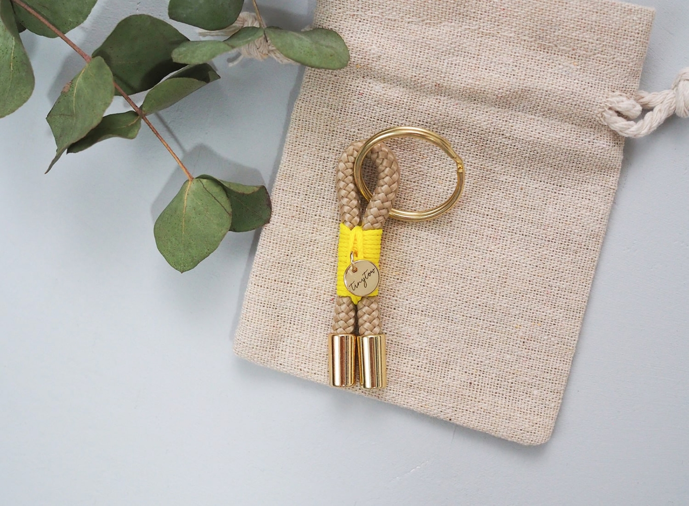 Schlüsselanhänger Towy aus beigefarbenem Tau mit leuchtgelber Takelung, goldenem Schlüsselring und Baumwollsäckchen.