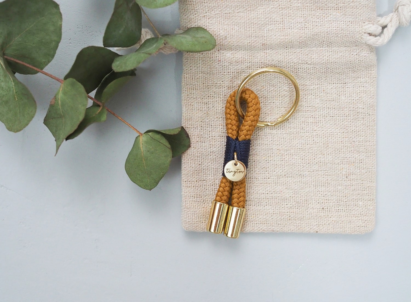 Schlüsselanhänger aus Tau in camel mit blauer Umwickelung (Takelung), goldenen Details und Leinen-Säckchen.