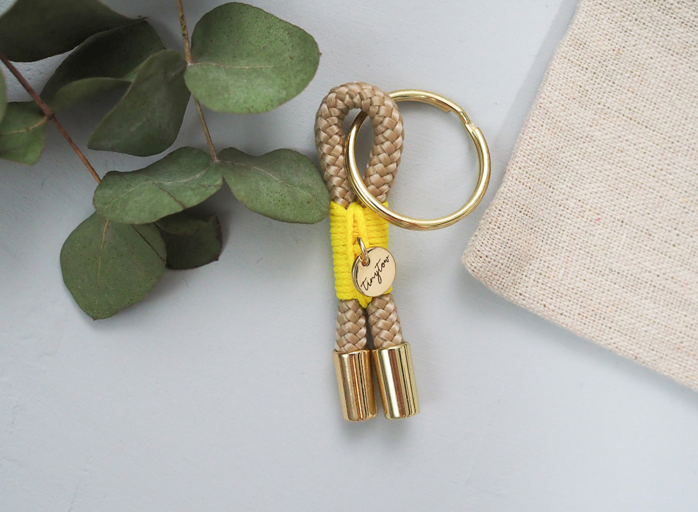 Schlüsselanhänger aus beigefarbenem Tau mit leuchtgelber Takelung, goldenem Schlüsselring und Baumwollsäckchen.