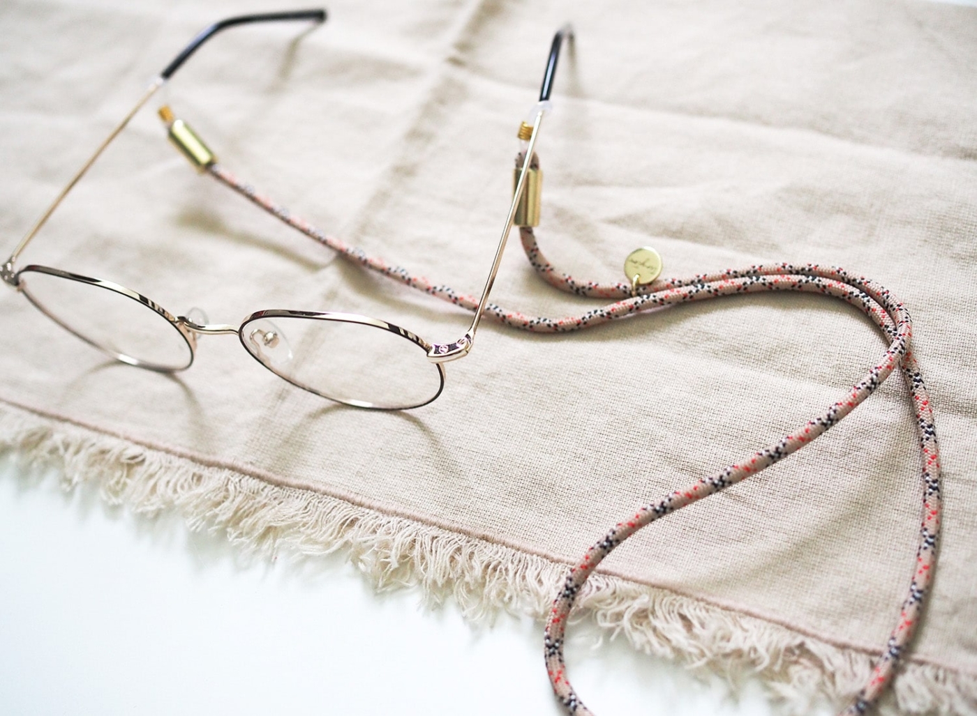 Brillenband aus Nylon-Tau in beige kariert an Brille mit goldenen Details.